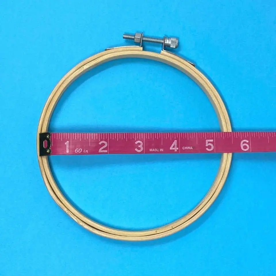 Bamboo embroidery hoop on light blue background with a pink measuring tape showing the hoop is five and a half inches in diameter