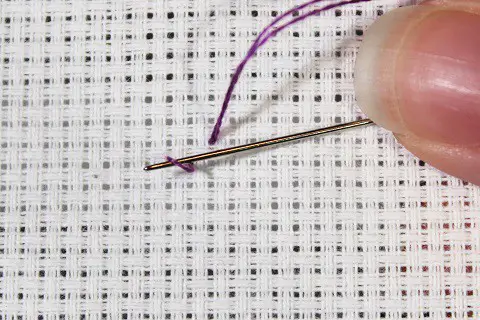 loop start for cross stitch with purple embroidery floss on white aida