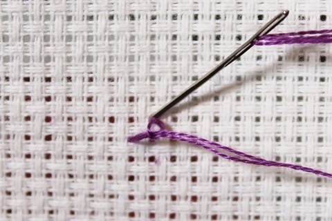 loop start in cross stitch by starting from the front done in purple embroidery floss on white aida