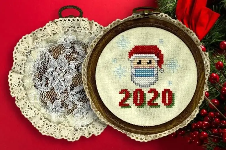 Two embroidery hoops, one showing the back with potpourri and lace, the other showing the front with a cross stitch of santa claus wearing a covid mask and the numbers 2020 over a red, holly berry background