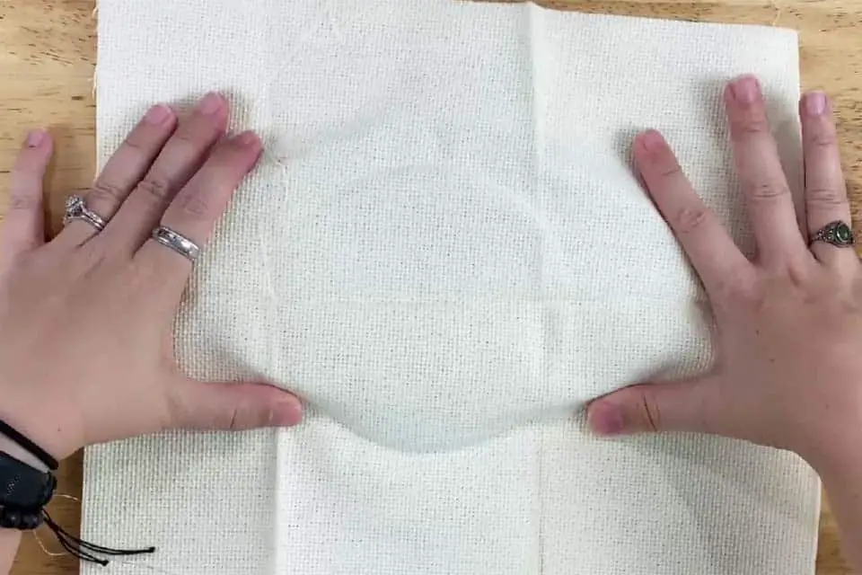 Two hands, open and pushing down on embroidery fabric so that a round shape can be seen from an embroidery hoop underneath.
