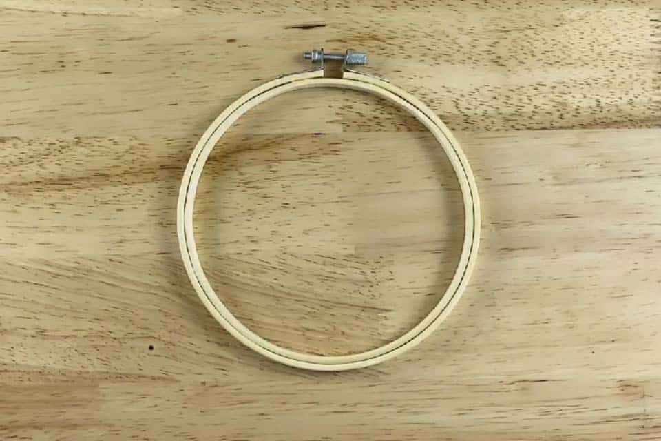 A wood embroidery hoop with chrome fastenings resting on top of a flat, wood surface