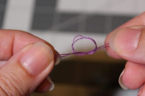 two hands tying a know with purple embroidery thread