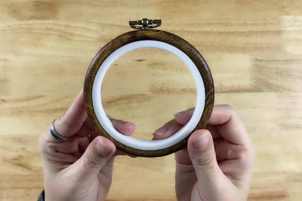 A wood-grain flexi hoop held in a pair of hands with a flat wood surface in the background